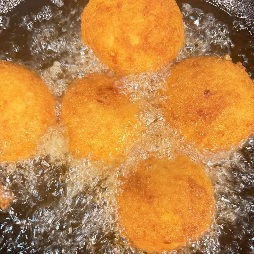 Five arancini turning golden in a pan of bubbling oil