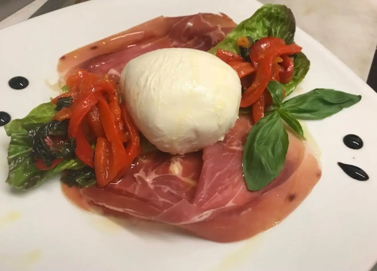 Burrata on prosciutto crudo with roasted peppers and basil