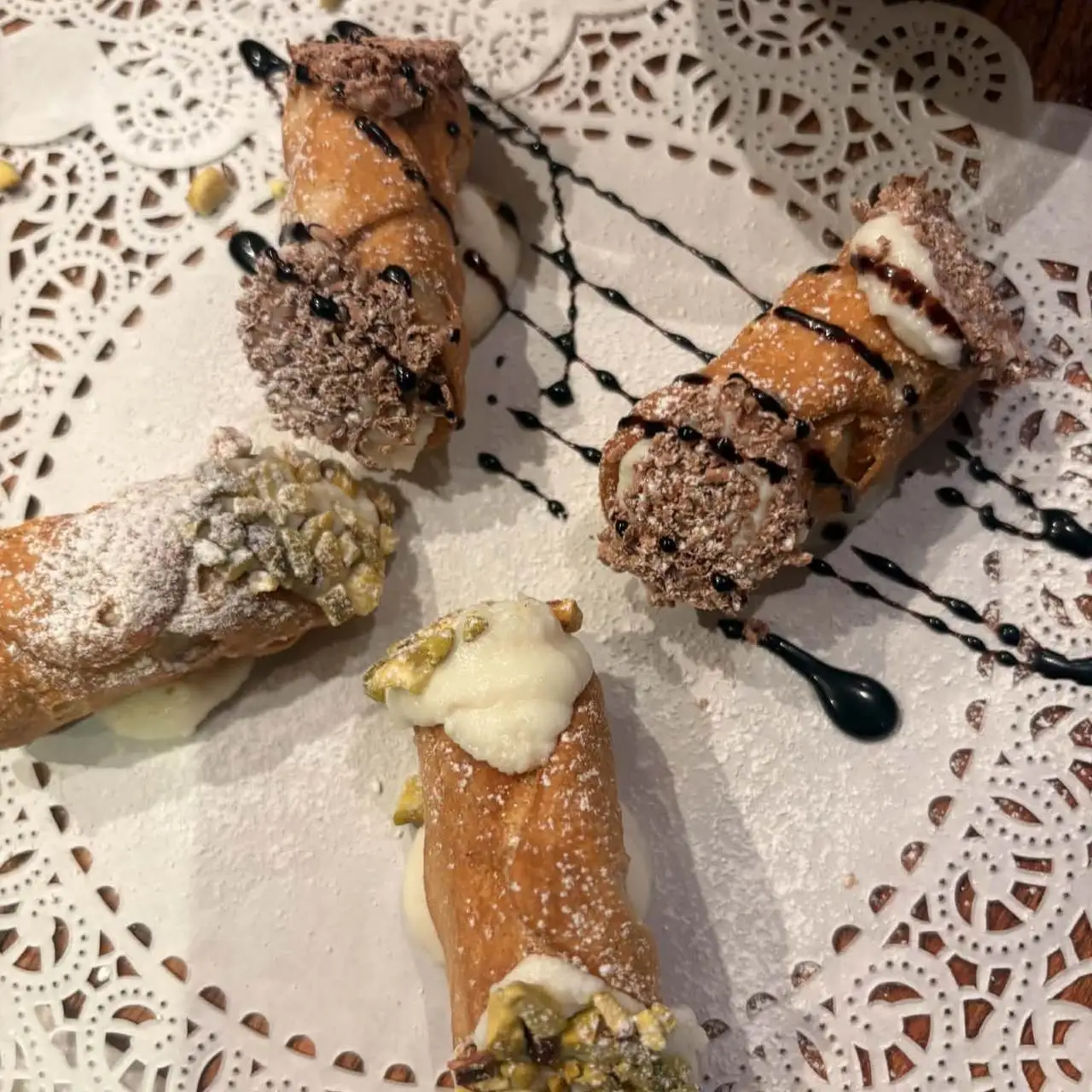 Four cannoli on a lace doily, two with pistachio ends and two with chocolate