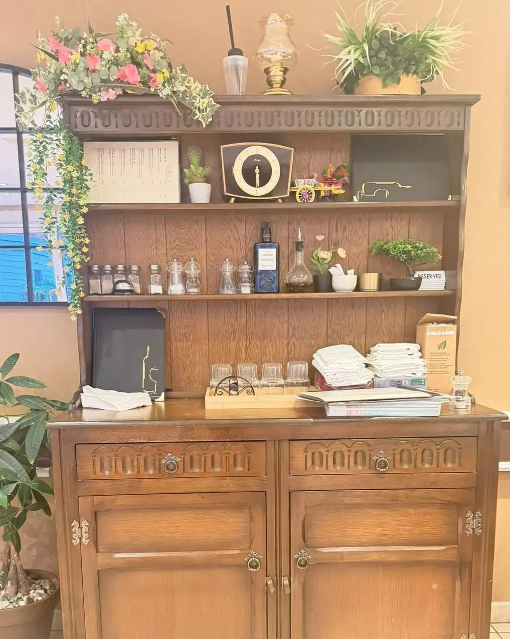 Shelves of a dark oak dresser with olive oil bottles, a mantel clock and a painted cart
