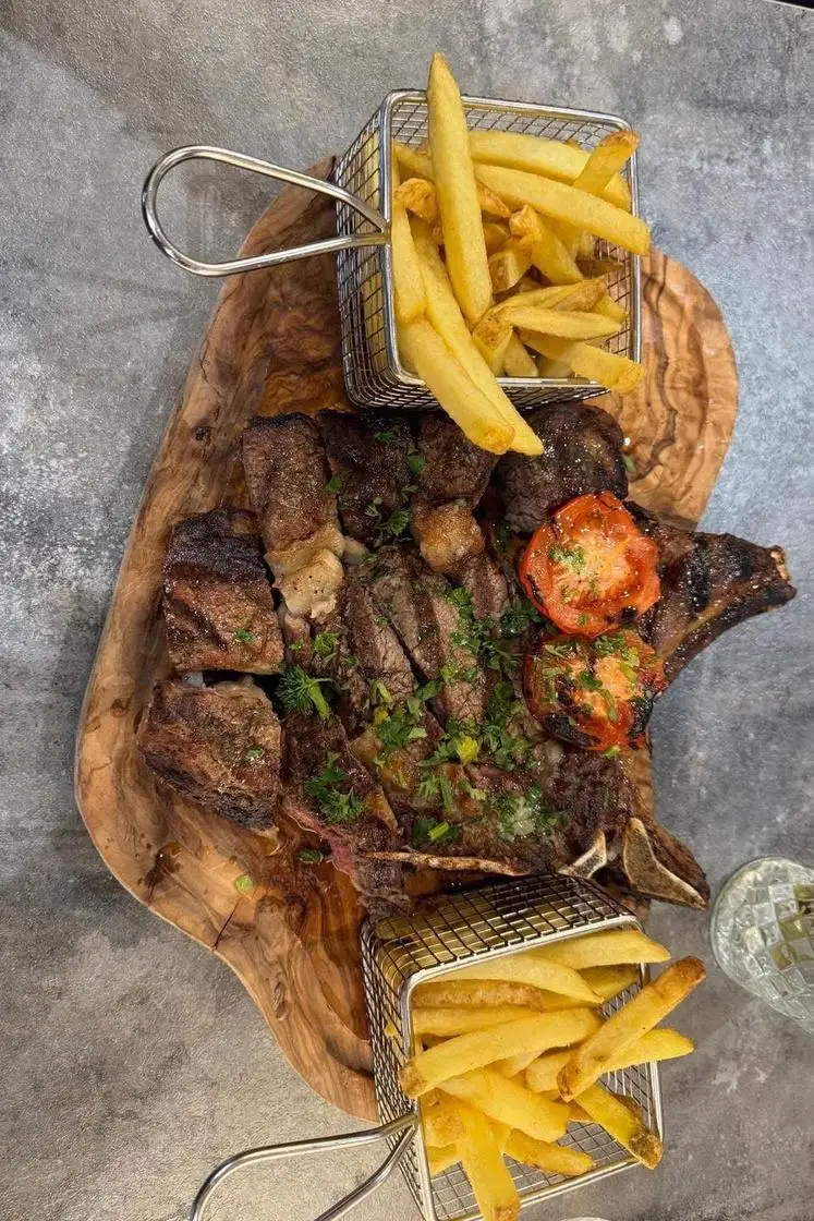 Sliced steak and chops on an olive-wood board with baskets of chips