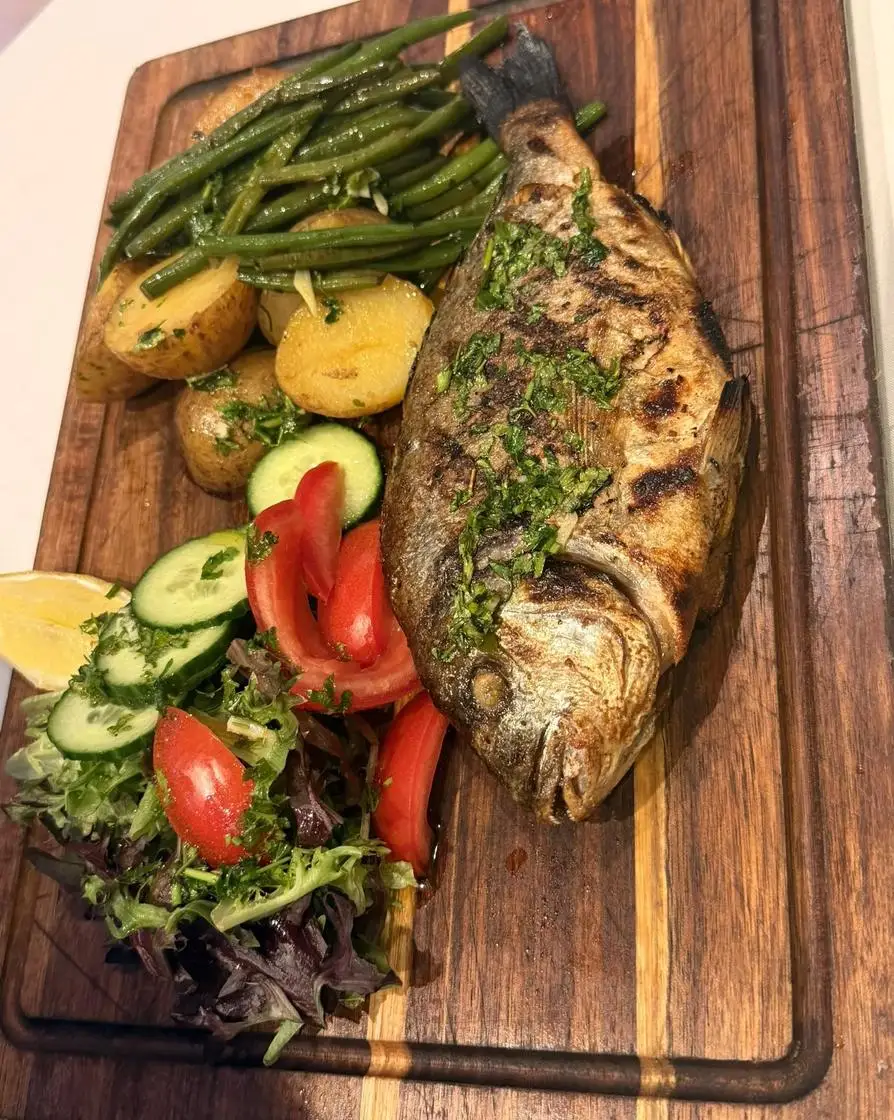 Whole grilled sea bream with green beans, new potatoes and salad on a wooden board