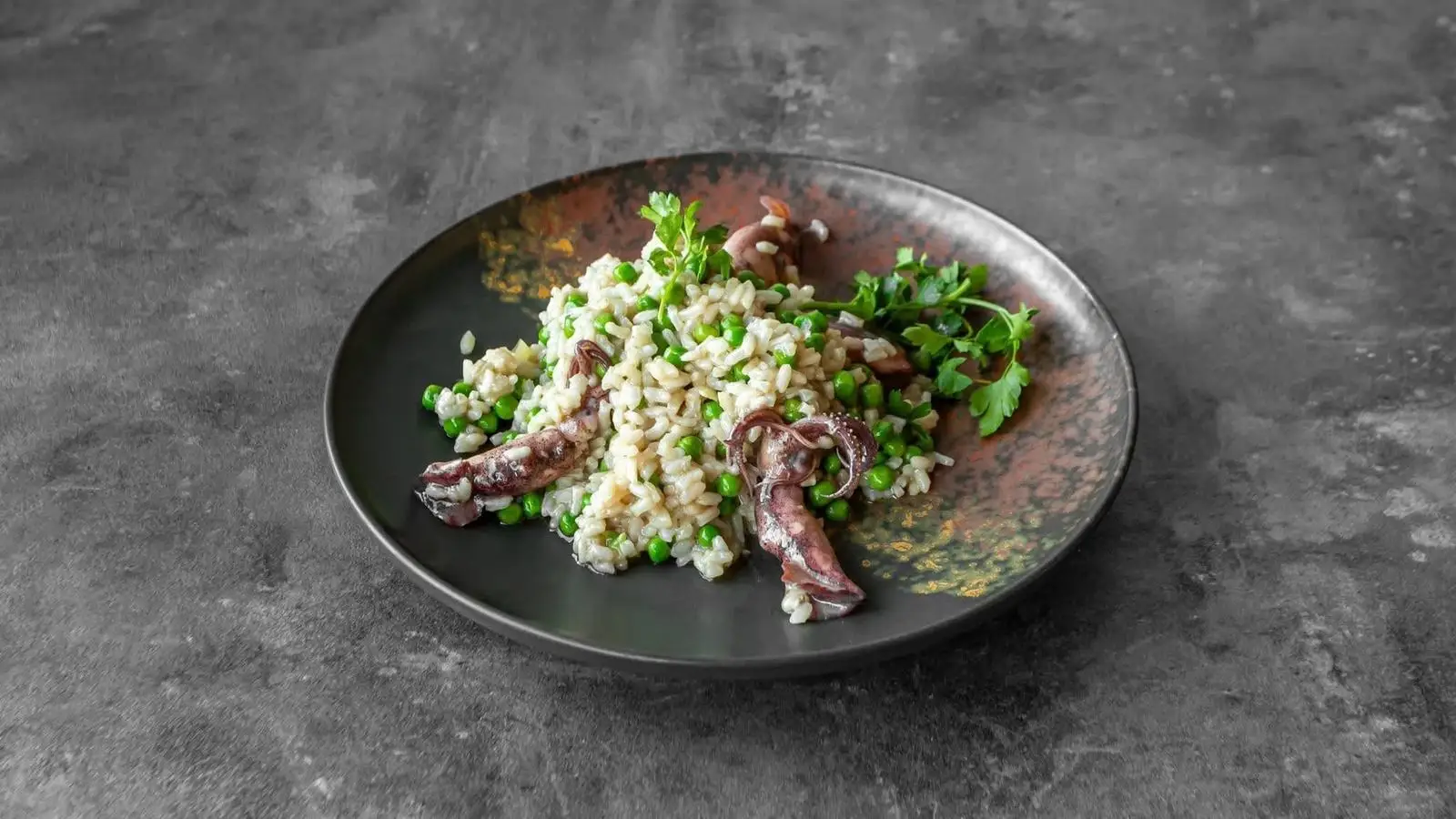 Creamy risotto with peas and whole baby squid on a charcoal plate