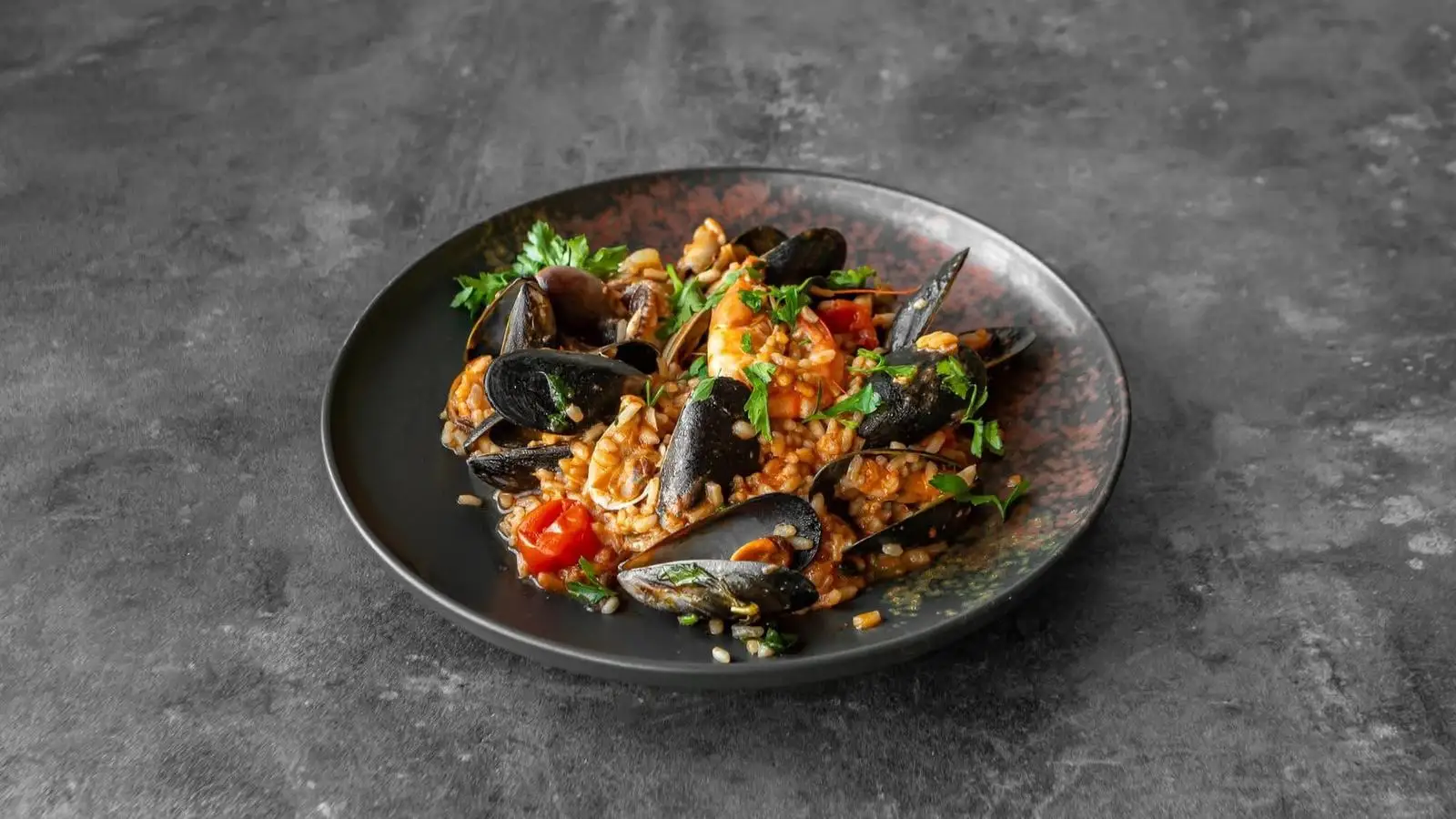Seafood risotto with mussels, king prawn and baby squid on a dark speckled plate