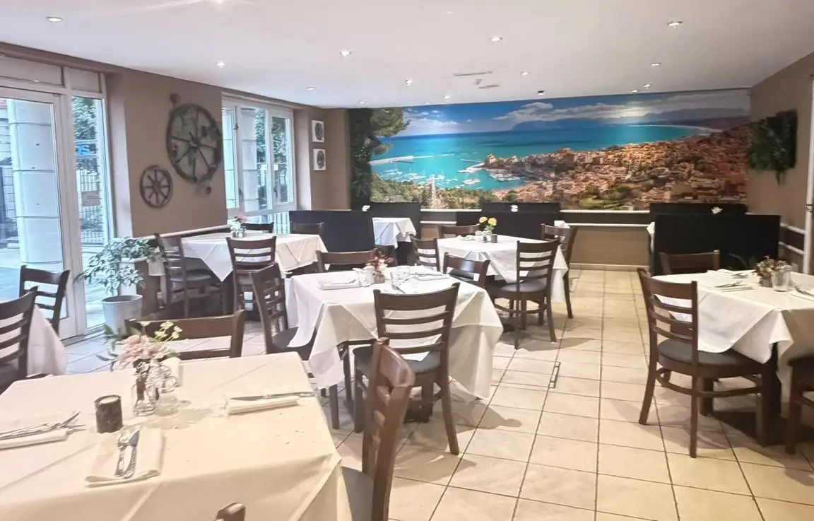 Dining room with cart wheels on the wall, white tablecloths and a panoramic mural of the Sicilian coast