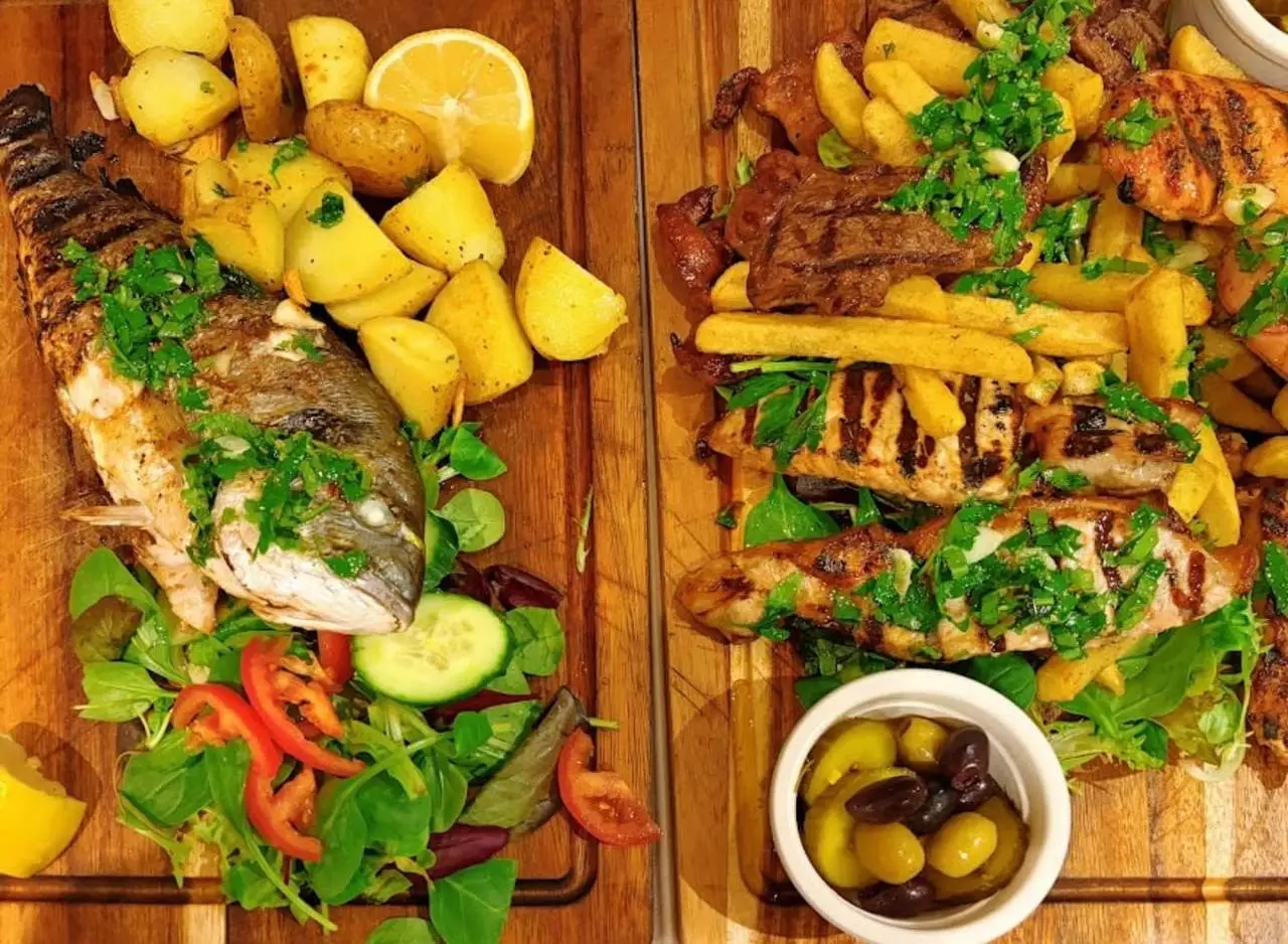 Two wooden boards, one with a whole grilled sea bream, one with mixed grilled meats and chips