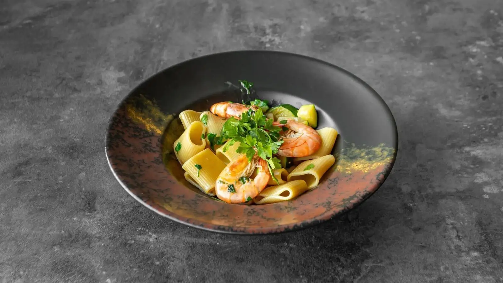 Paccheri pasta with king prawns and courgette in a copper-rimmed bowl
