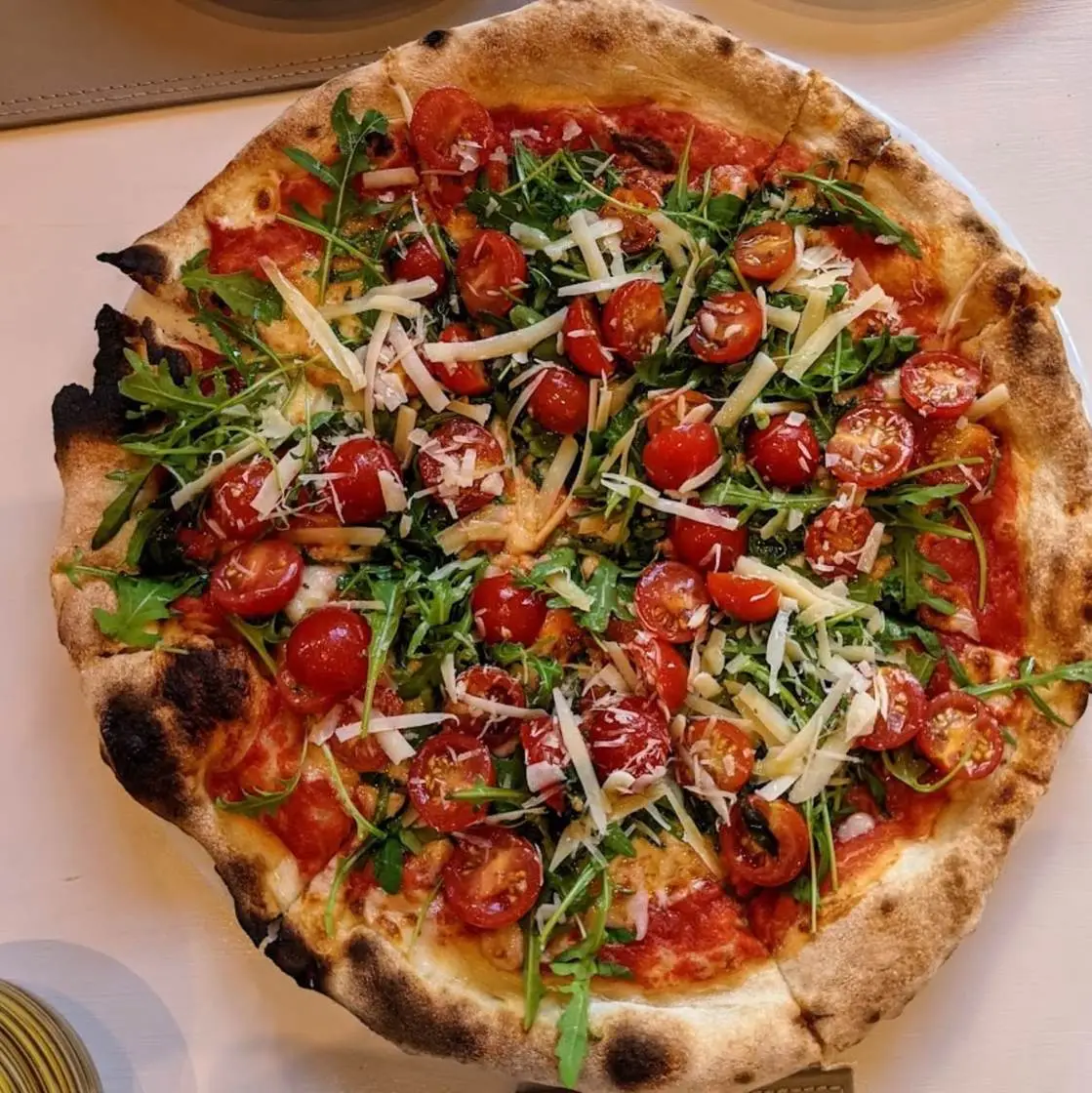 Blistered pizza topped with cherry tomatoes, rocket and shaved Grana